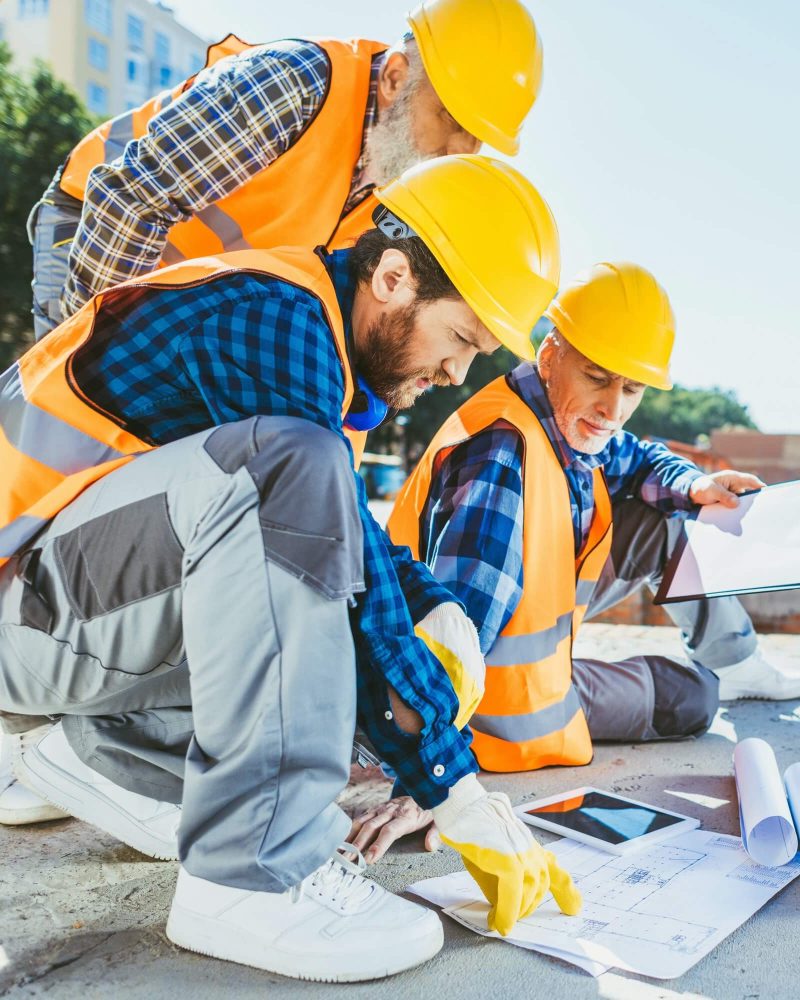 handsome-construction-workers-sitting-on-concrete-at-construction-site-discussing-building-plans-1.jpg