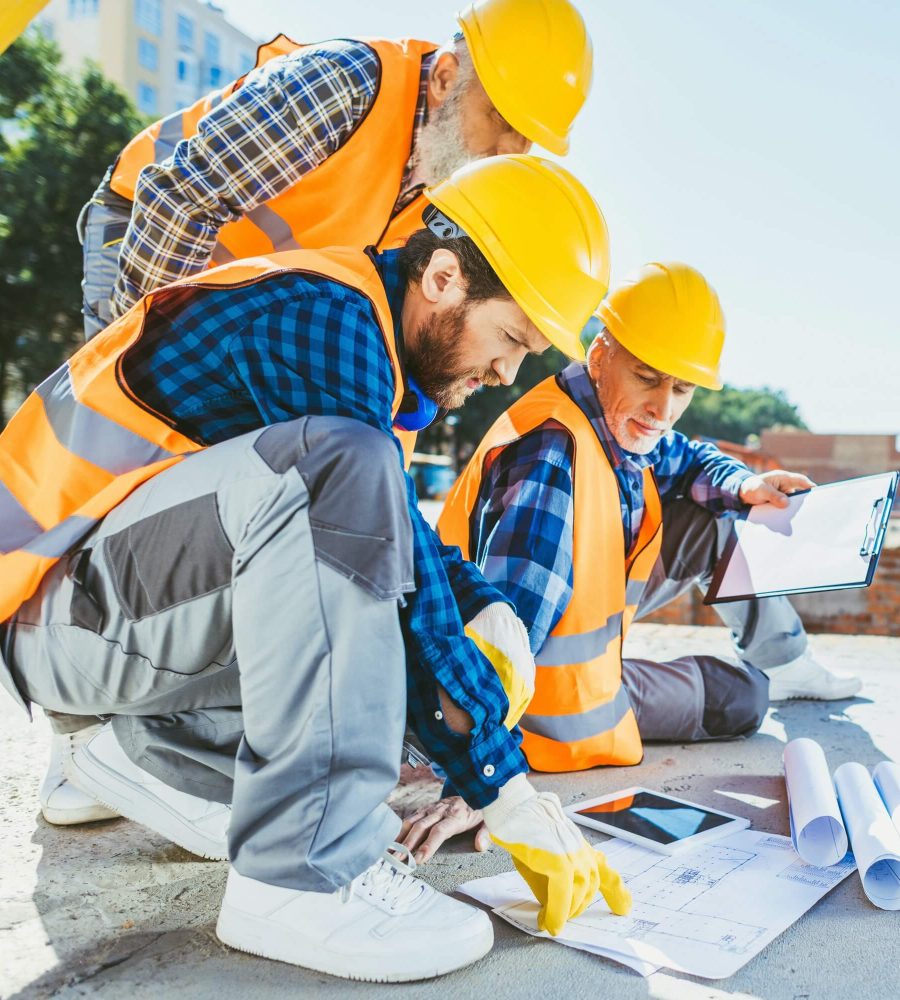 handsome-construction-workers-sitting-on-concrete-at-construction-site-discussing-building-plans-1.jpg