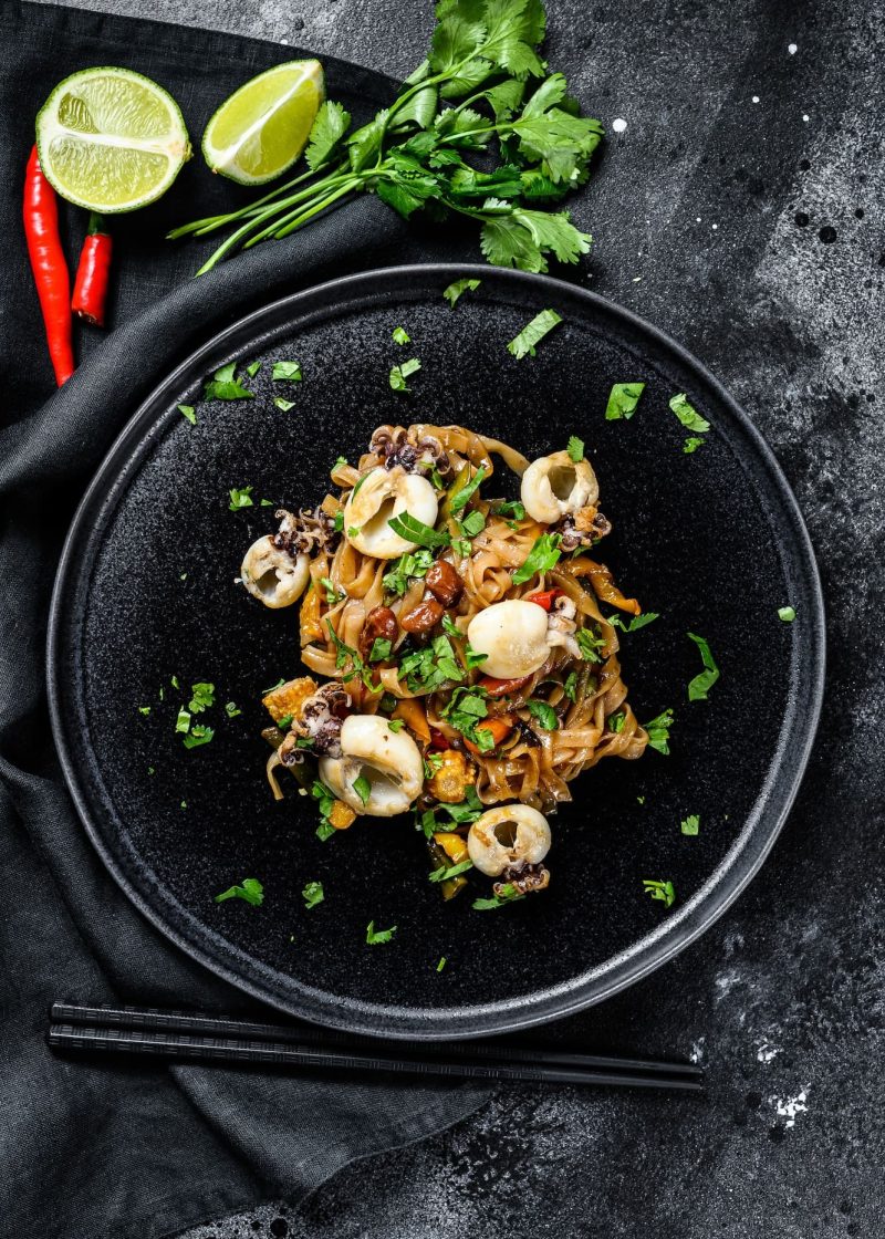 homemade-stir-fry-damage-noodles-with-seafood-and-vegetables-in-a-plate-black-background-top-view.jpg