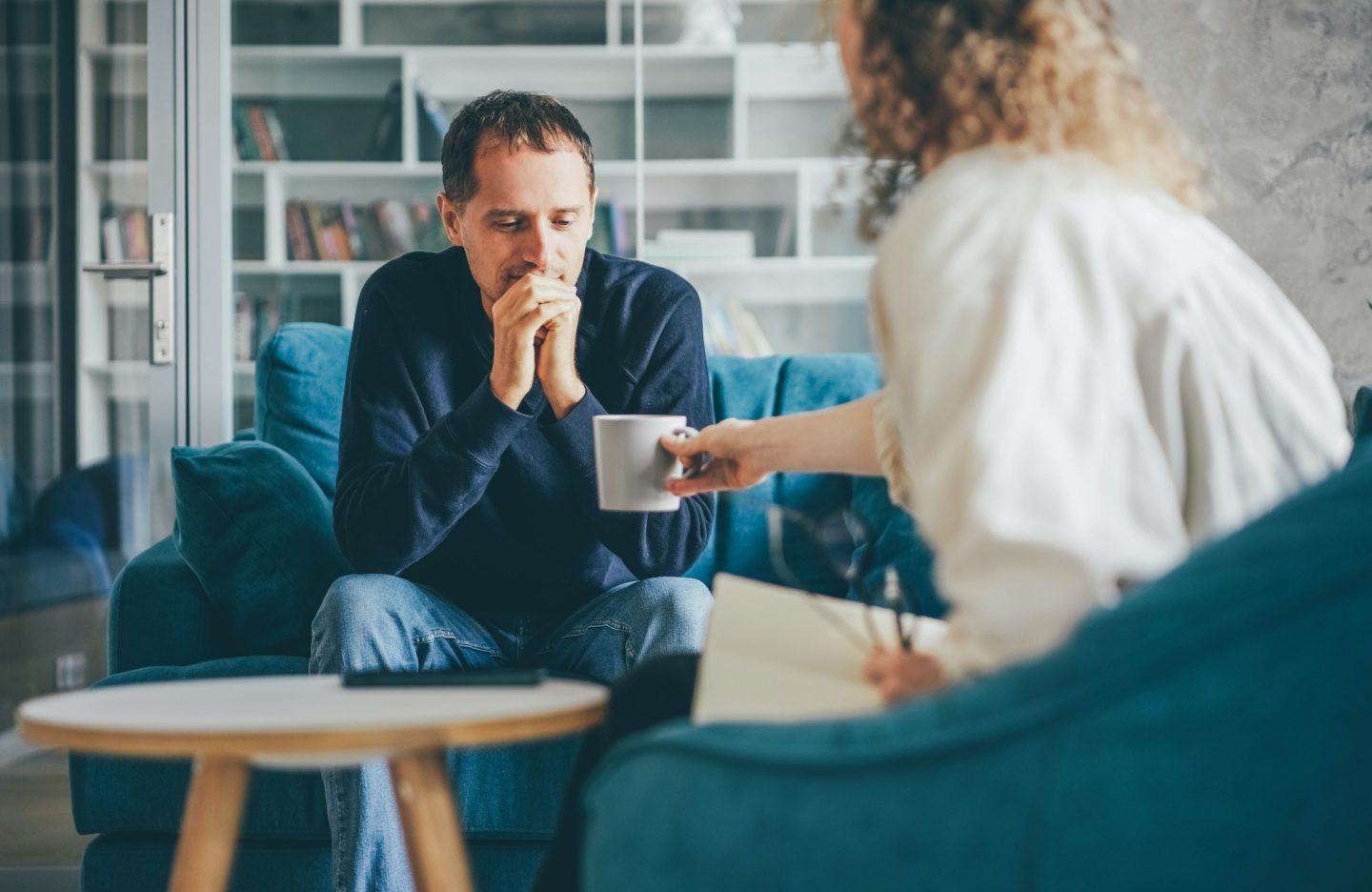 curly-haired-woman-consultant-offers-cup-of-coffee-to-stressed-man-client.jpg