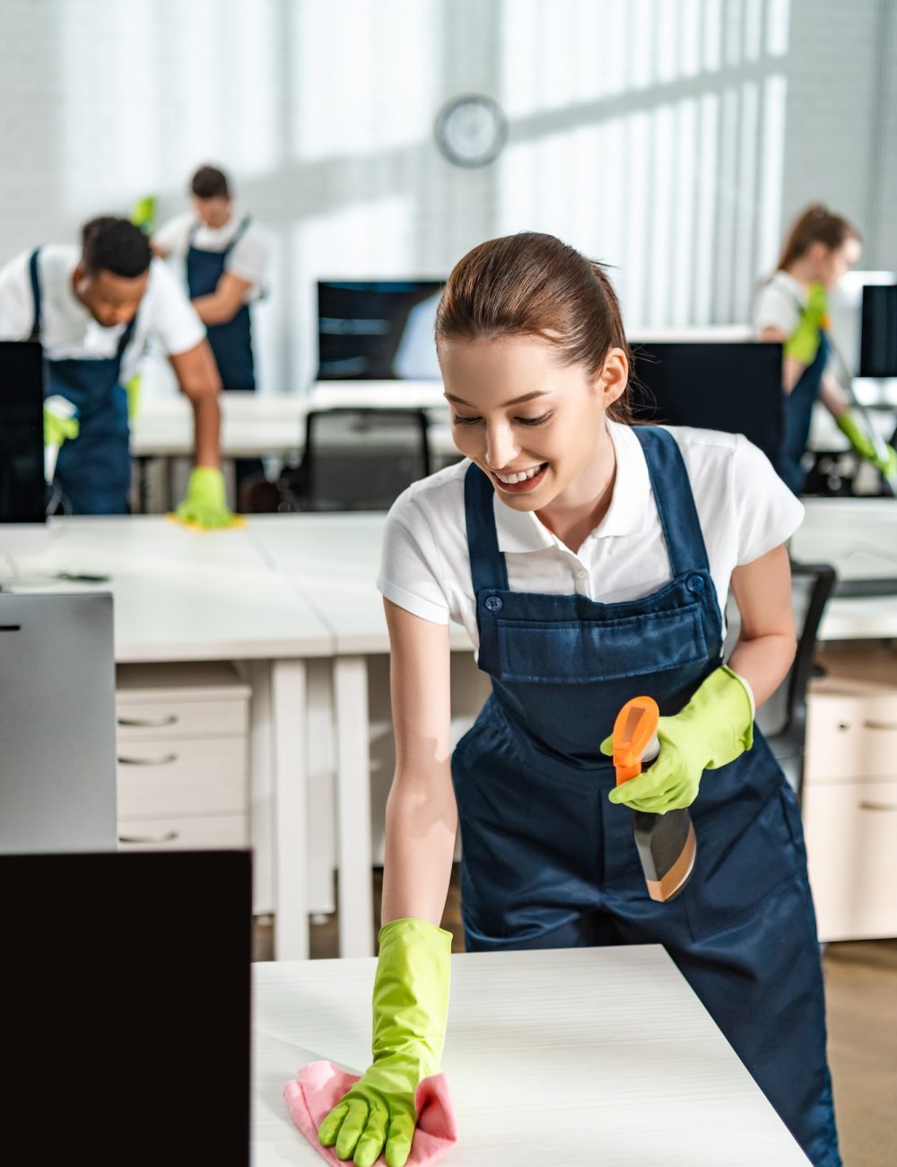 cheerful-cleaner-in-overalls-cleaning-office-desk-with-rag.jpg